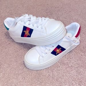 White shoes with red green and a gold bee symbol.